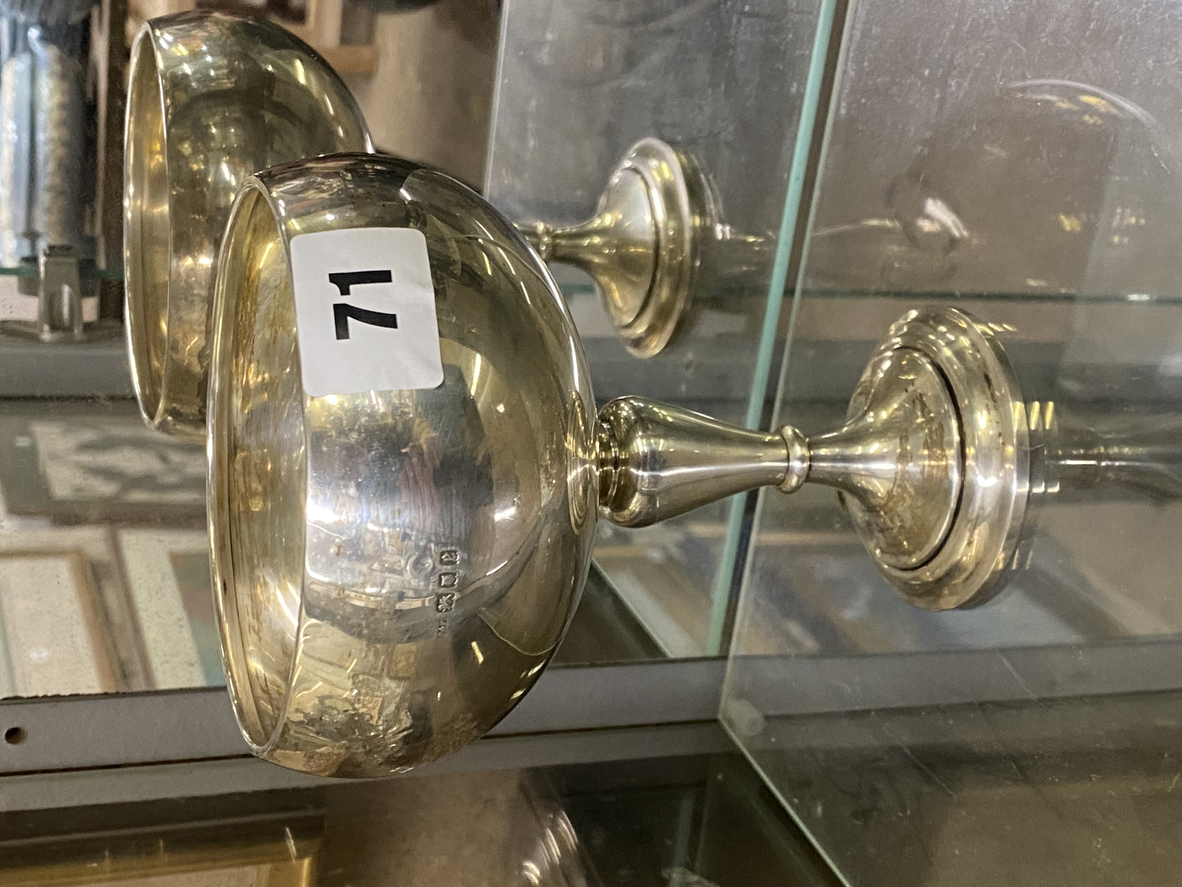 A reflective silver goblet with a numbered sticker reading '71,' placed on a glass shelf.